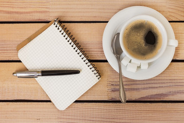 cup of coffee and a notepad with pen on wooden background