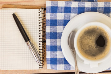 cup of coffee on a napkin and notepad with pen on wooden background