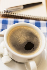 cup of coffee on a napkin and notepad with pen on wooden background