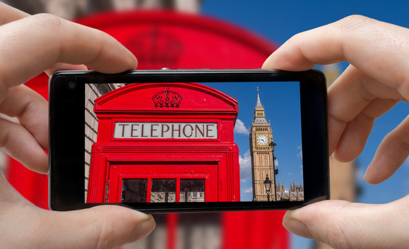 Tourist is taking photo of red phonebooth in London with smartphone.