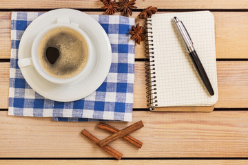 cup of coffee on a napkin and notepad with pen on wooden background
