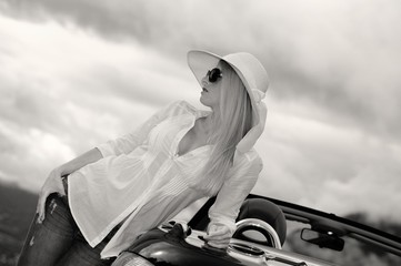 Junge blonde Frau mit Sonnenbrille, Hut und Cabrio