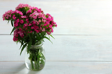 a bouquet of chrysanthemum in a glass jar with water on a white wooden background