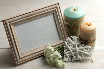 a bouquet of chrysanthemum with wooden frame for photo on wooden background with decorative white heart near the two candles