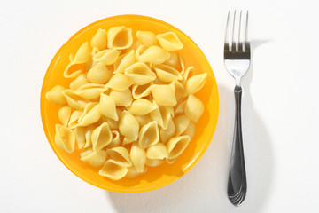 Cooked macaroni shells, served without sauce an orange plate on white background. Close up, top view, high resolution product.