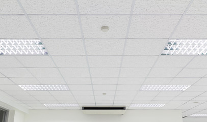 Office ceiling in perspective with white texture of acoustic gypsum plasterboard, lighting fixtures or fluorescent panel light suspended on square grid structure. Interior modern building background. - obrazy, fototapety, plakaty