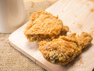 fried chicken on a chopping broad with a glass set on a sack background