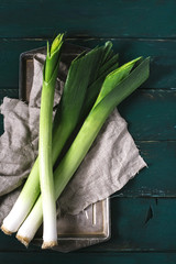 Leek and scissors on a light textile and metal plate on a dark background of the aged wooden boards vintage vertical top view