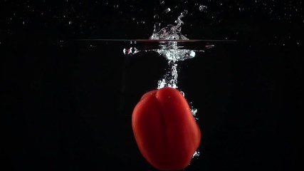 Red bell pepper falling down in water, black background super slow motion shot - Powered by Adobe