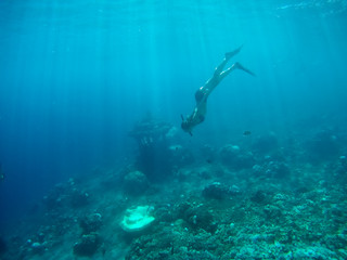 Fototapeta na wymiar Underwater shot of the woman moving on the breath hold in the depth. Amed village, Bali, Indonesia