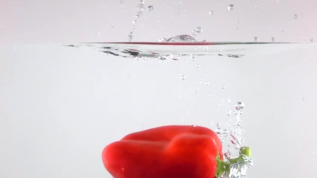 Red bell pepper falling down in water, light background super slow motion shot