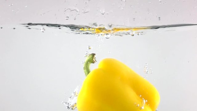 Super slow motion shot of yellow bell pepper falling down in water