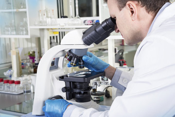 Naklejka na ściany i meble Portrait of caucasian male chemist scientific researcher using microscope in the laboratory interior