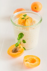 Ein Glas frisch gekochter Milchreis mit Aprikosen steht auf einem weißen Tisch.