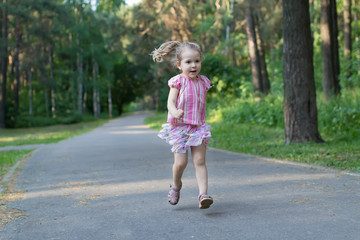 Fototapeta premium Blonde three years old girl running on asphalt park footpath