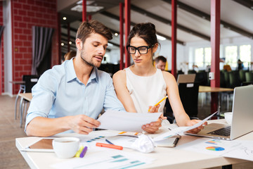 Serious young business man and woman working together in office