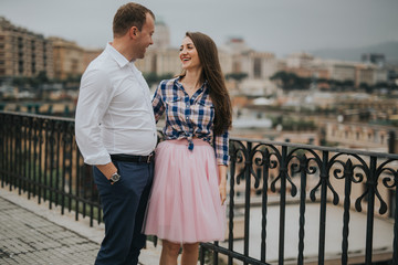 Young cute couple honeymoon posing in the street holding their hands on dating in a beautiful place italy near ocean and mountains, hug, smile and talk to each other
