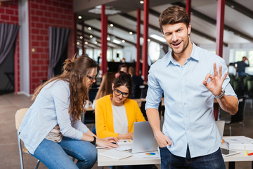 Happy successful young businessman standing and showing ok sign