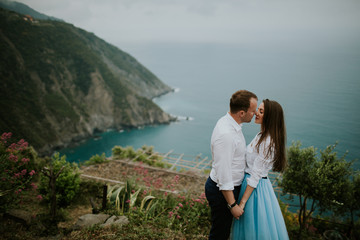 Fototapeta na wymiar Young cute couple honeymoon posing and holding their hands on dating in a beautiful place italy near ocean and mountains, hug, smile and talk to each other 