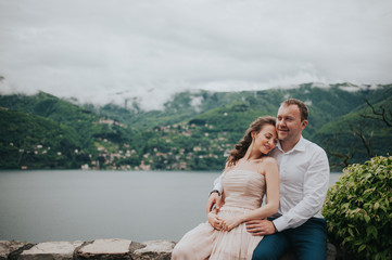 Young cute couple honeymoon walks holding their hands on dating in a beautiful place italy near ocean and mountains, hug, smile and talk to each other