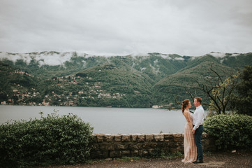 Fototapeta premium Young cute couple honeymoon walks holding their hands on dating in a beautiful place italy near ocean and mountains, hug, smile and talk to each other