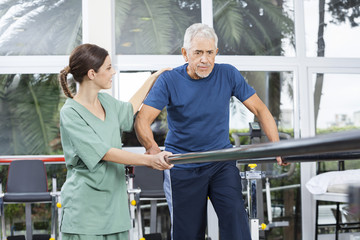 Fototapeta na wymiar Female Physiotherapist Motivating Senior Patient To Walk Between
