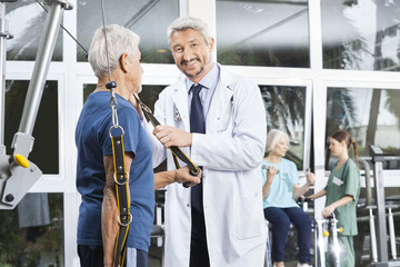 Happy Mature Doctor Assisting Senior Man With Resistance Band