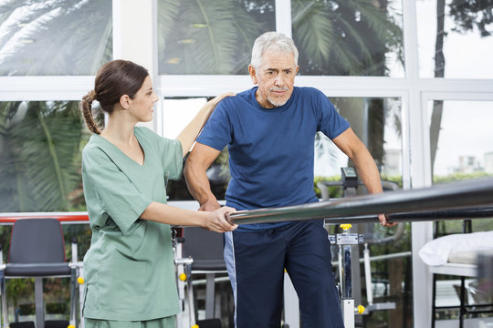 Female Physiotherapist Motivating Senior Patient To Walk Between