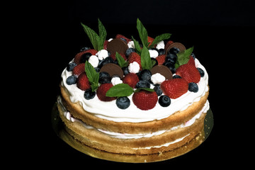 Biscuit homemade cake with cream and berries on black background