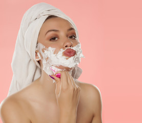 beautiful young woman shaving her face with foam and razor