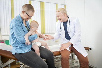 Baby Touching Doctor's Hand While Sitting On Mother's Lap