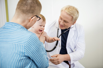 Doctor Examining Crying Baby Held By Mother