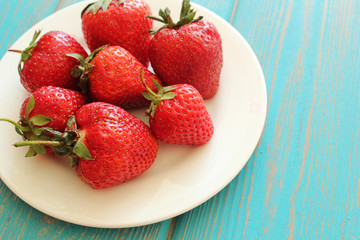 Strawberries in white plate on wooden blue desk.