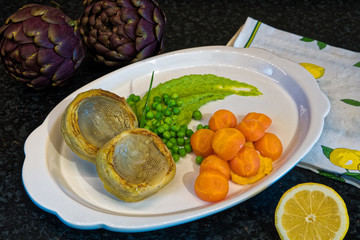 Plate of cooked artichokes, served with peas and carrots