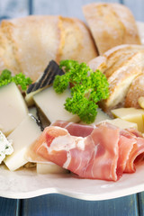 prossiutto with cheese and bread on white plate on blue wooden background