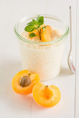 Ein Glas frisch gekochter Milchreis mit Aprikosen steht auf einem weißen Tisch.