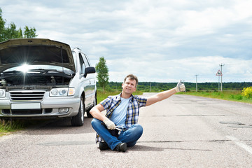 Man with tools showing thumbs up near his broken car