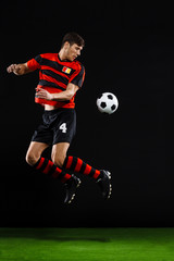 Fototapeta na wymiar Soccer player kicking ball over black background