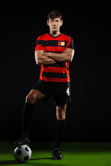 Soccer player with ball standing over black background