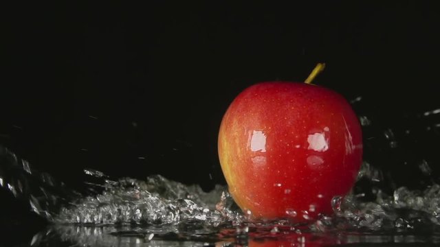 SLOW MOTION: A water flow falls on a red apple on a black background
