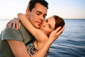 Fototapeta premium Happy beautiful couple walking and embracing on the beach of the sea at sunset