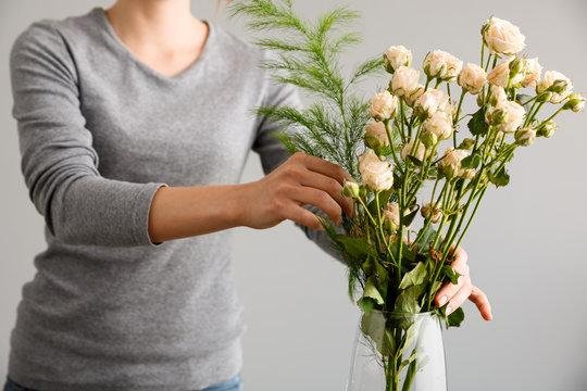 Fototapeta Girl make bouquet over gray background, putting flowers in vase.