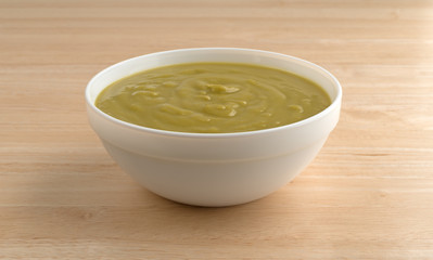 Bowl of green pea soup on a wood table top illuminated with window light.
