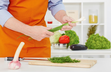 Mid section of a man preparing to chop .green onions in the kitchen at home.
