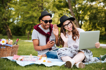 Couple with laptop listening to music from smartphone in park