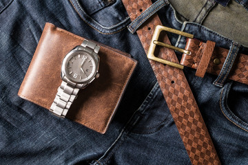 Top view of wallet and wrist watch on blue jeans with leather be