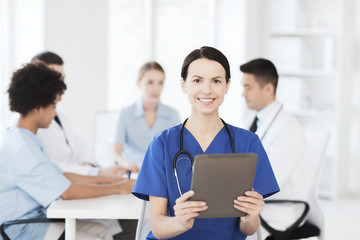 Fototapeta premium happy doctor with tablet pc over team at clinic