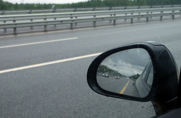 Riding cars reflected in car side mirror on suburban highway in rainy weather