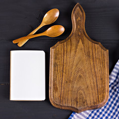napkin, a recipe book, a cutting board and a wooden spoon on a black background
