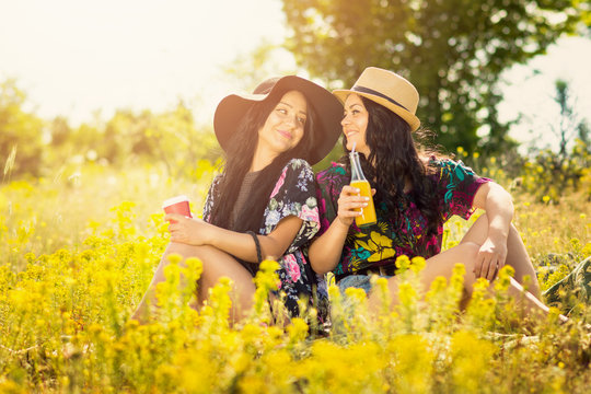 Two boho sisters drinking juice and coffee outdoors on sunny summer day